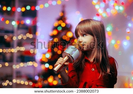
Happy Girl Holding a Microphone Singing Carols. Cheerful child performing Christmas songs for her family at home
