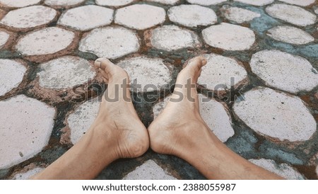 Close-up photo of a pair of feet with heels touching against a hexagonal paving background. Selective focus. Lifestyle concept