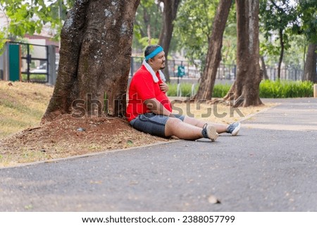 Picture of young fat man having heart pain after running while sitting in the park
