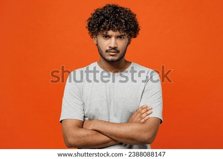 Young sad frowning mad furious shrewd Indian man he wearing t-shirt casual clothes hold hands crossed folded looking camera isolated on orange red color background studio portrait. Lifestyle concept Royalty-Free Stock Photo #2388088147