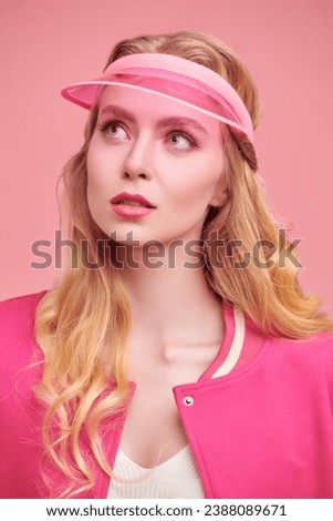 Trendy pink color. A beautiful blonde  girl poses in a pink visor and a pink bomber jacket on a pink studio background. Copy space. Youth girlish sports style. 