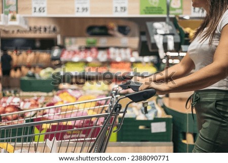 Unrecognizable young woman passing by with her metal cart doing the weekly shopping in the supermarket.Youthful weekly shopping concept. Royalty-Free Stock Photo #2388090771