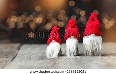 three Christmas gnomes on a wooden table against a background of defocus lights