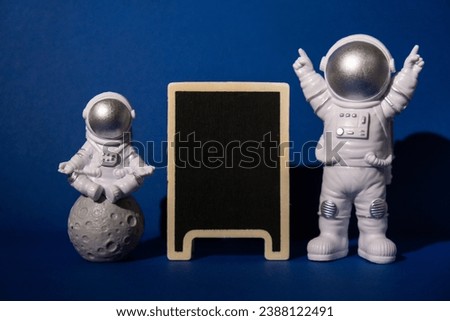 Plastic toy astronaut with blackboard template mock up for your text on colorful blue background Copy space. Concept of out of earth travel, private spaceman commercial flights missions and