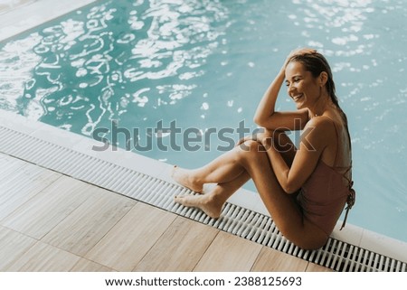Pretty young woman relaxing by the indoor swimming pool Royalty-Free Stock Photo #2388125693
