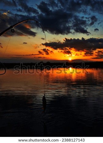 Fishing at sunset. Catching predatory fish on spinning. Sunset colors on the water surface, sunny path from the low sun. Perch caught on yellow spoonbait Royalty-Free Stock Photo #2388127143