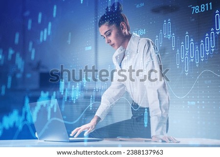 Attractive young female working on desk with glowing candlestick forex chart on blurry office interior background. Stock market and investment concept. Toned image. Double exposure
