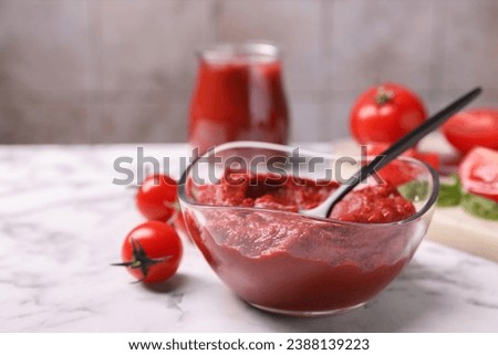 Glass bowl of tasty tomato paste with spoon and ingredients on white marble table, closeup. Space for text Royalty-Free Stock Photo #2388139223