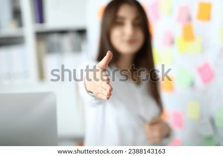 Focus on tender woman arm reaching to shake hands with someone in modern workplace with white board and colorful sticker. Art design project. Blurred background