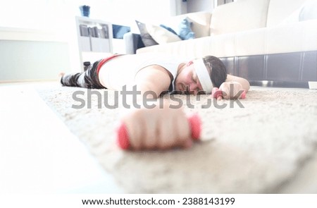 Tired Man Lying on Floor with Dumbbells in Hand. Exhausted Sportsman Sleep in Apartment After Fitness Training for Weight Loss. Overweight Guy Holding Sports Equipment. Young Beard Guy in Sportswear