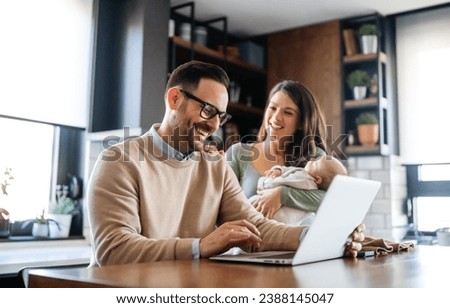 Young father works on laptop while his wife looks after child.Work from home parenting telecommuting