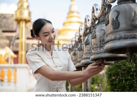 A beautiful Thai-Asian woman in a traditional Thai-Northern dress is ringing temple bells in a temple, making a wish and making a merit on a Buddhist holy day. Thai-culture, Buddhist