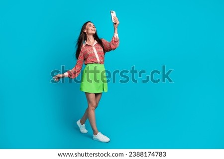 Full body photo of pretty young girl hold device walk take selfie dressed stylish green skirt isolated on aquamarine color background