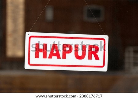 White an red sign hanging at the glass door of a shop saying in Albanian: "Hapur", meaning in English "Open".