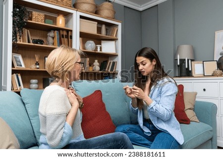 Young nervous overjoyed woman holding a pregnancy test tells her mom that she is pregnant and will have a baby. Future grandmother and mother happy at home on sofa looking at test