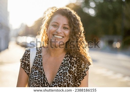 Portrait of a smiling young woman with curly hair in the city
 Royalty-Free Stock Photo #2388186155