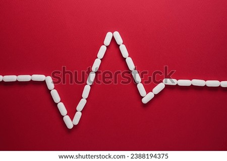 Heart rhythm cardiogram wave made of medical pills against a red background. PQRST sinus rhythm shape formed from white tablets. Top view, flat lay. Space for text.