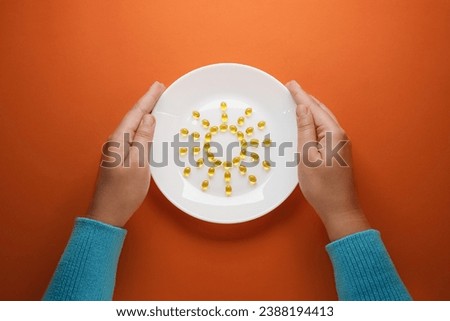 Top view female hands holding  round plate with Cod Liver Oil Capsules, Omega 3, Vitamin D in the sun shape on orange background. Flat lay, top view, space for text. 