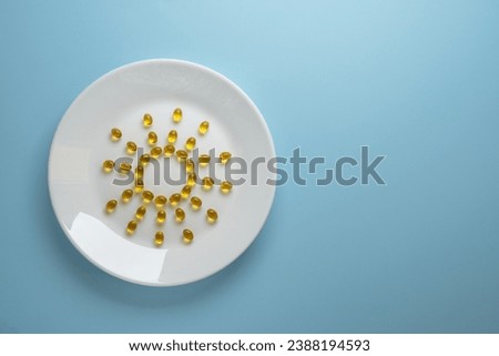 Top view of white plate with Vitamin D in the sun shape on an blue background. Concept of nutritional supplement and health. Creative composition. Flat lay. Space for text. 