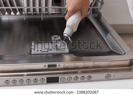 female hand pours rinse aid into the dishwasher compartment in modern white kitchen Royalty-Free Stock Photo #2388202687