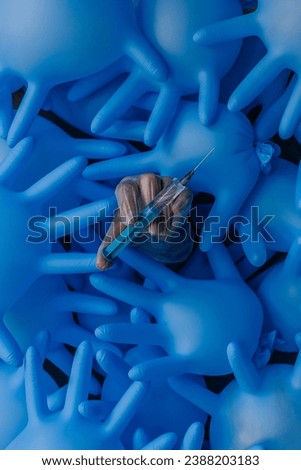 background of inflated blue medical latex gloves, in the center is the hand of a woman in a transparent glove with a syringe