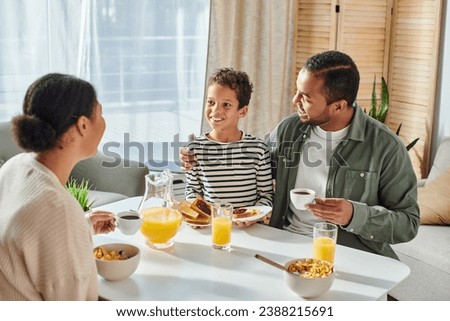 happy joyful african american parents looking lovingly at their little son at breakfast table