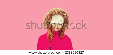 Winter portrait of happy smiling little girl child in jacket with hood on pink background