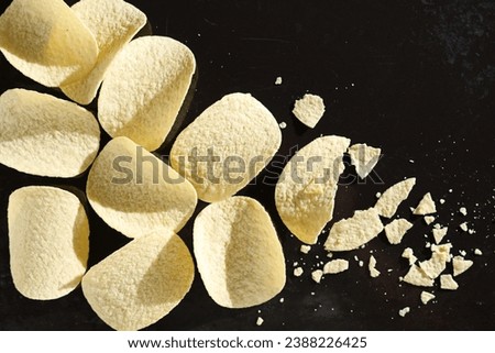 Tasty potato chips whole end broken on a black tray background, top view. Good snack for beer Royalty-Free Stock Photo #2388226425