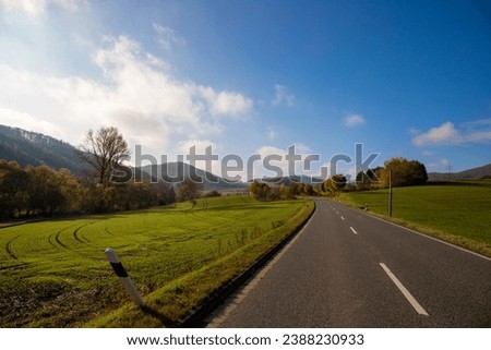 Panoramic view on a road with green meadows blue sky, in autumn with forest