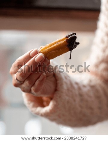 A person's hand holding a freshly dipped churro with dripping chocolate sauce, embodying a moment of sweet indulgence Royalty-Free Stock Photo #2388241729