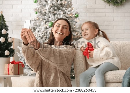 Happy young mother and her little daughter taking selfie at home on Christmas eve