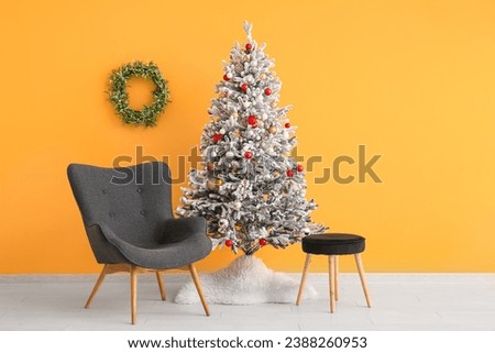 Beautiful Christmas tree with comfortable armchair near orange wall
