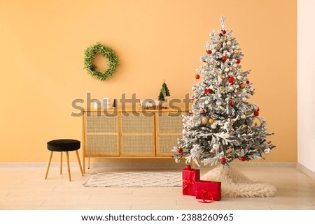 Beautiful Christmas tree with gift boxes and chest of drawers near beige wall