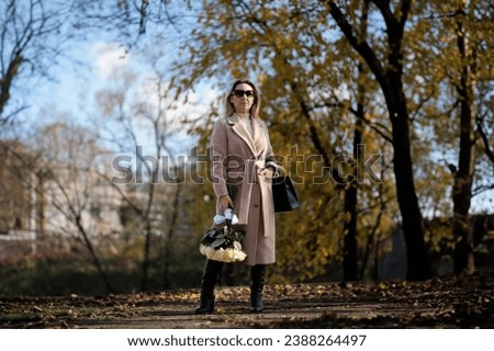 In the autumn park, a business woman is holding a bouquet of white roses Stylish woman in a coat in autumn with a bouquet of white roses.