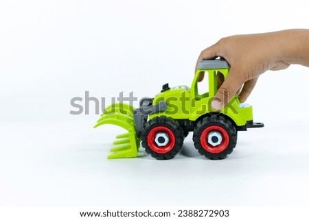 Close-up of a kid hand playing with the car close on a white background. Plastic child toy on white backdrop. Construction vehicle. Children's toy. Tractor Toy.
