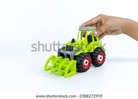 Close-up of a kid hand playing with the car close on a white background. Plastic child toy on white backdrop. Construction vehicle. Children's toy. Tractor Toy.