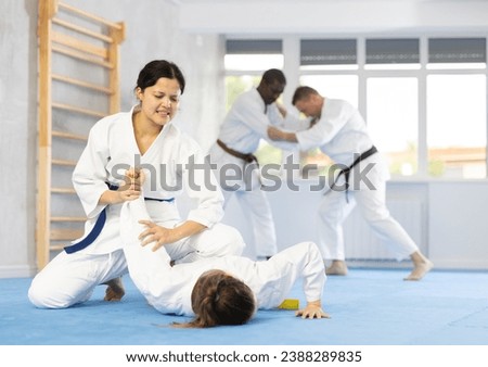 Adult woman and young female judoka practicing judo technique in group in gym