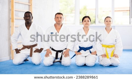 Serious middle-aged judo practitioners in kimono sitting in seiza pose in row in sports hall