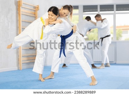 Willing middle-aged woman attendees of judo classes wrestling in pairs in sports hall