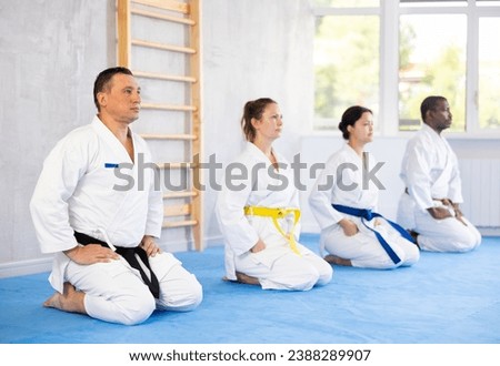 Calm middle-aged male attendee of karate classes sitting in seiza position in group during workout session