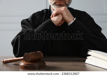 Judge with gavel and book sitting at wooden table indoors, closeup