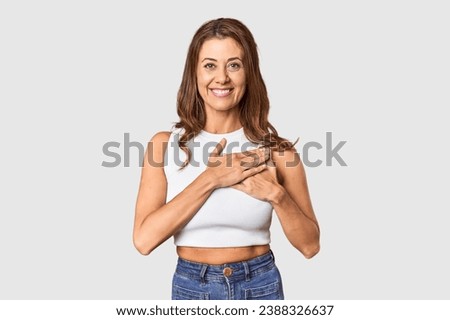 Middle-aged woman portrait in studio setting has friendly expression, pressing palm to chest. Love concept.