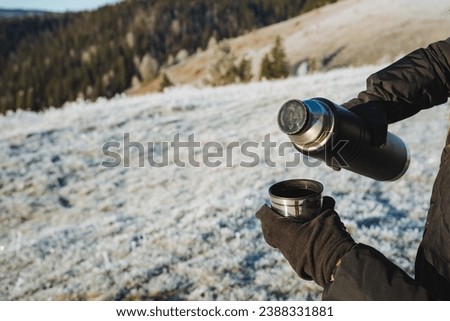Thermos with hot tea in nature in winter, man holding mug and thermos in hands, picnic in nature. High quality photo