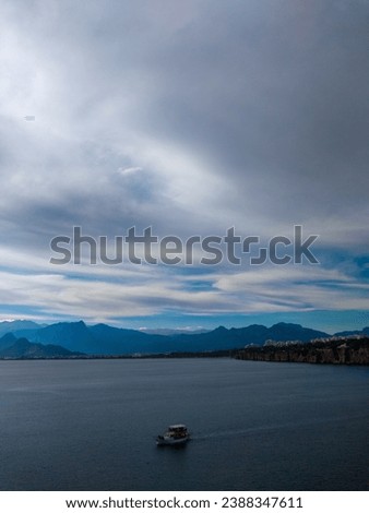 This is a picture of a scenic view of a boat on a lake surrounded by mountains. The boat is white and has a blue roof and windows. It looks like a tourist boat that takes people on sightseeing trips. 