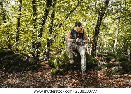 young and beautiful photographer resting on a stone in the forest after walking and photographing the wonders of the environment, while looking at the photographs in the camera