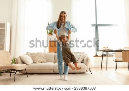 young mother dances with her little son at home and holds hands, woman plays with her child in the room, 2 year old boy flies and rejoices in the arms of his parent