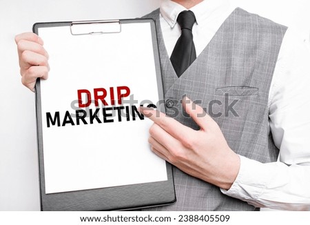 DRIP MARKETING inscription on a notebook in the hands of a businessman on a gray background, a man points with a finger to the text