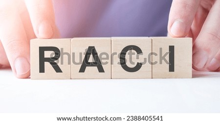 Businessman hand holding wooden cube block with RACI business word on table background.