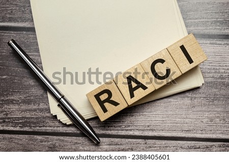 RACI word on wooden block and pen with papers on wooden background Royalty-Free Stock Photo #2388405601