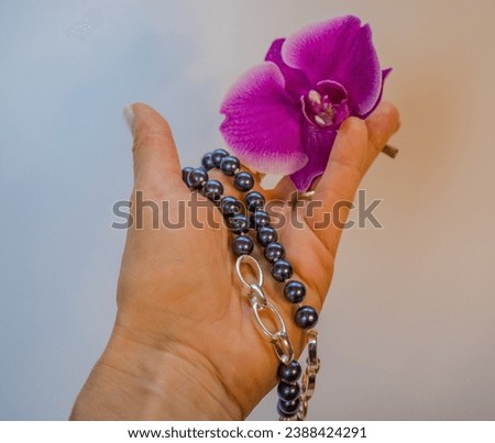 Black pearl beads in a woman's hand with purple orchid on a white background